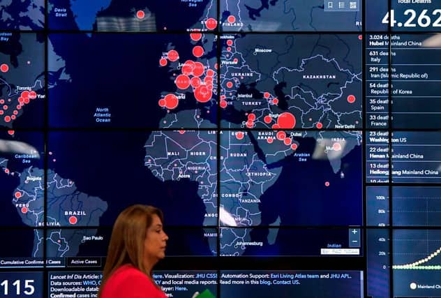 A woman passes by a world map showing countries infected with the coronavirus (Photo by LUIS ACOSTA/AFP via Getty Images)