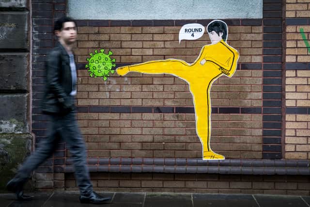 A member of the public walks past a piece of street art by 'Palley' that features Bruce Lee kicking a coronavirus molecule in Glasgow's East End. Picture: Jane Barlow/PA Wire