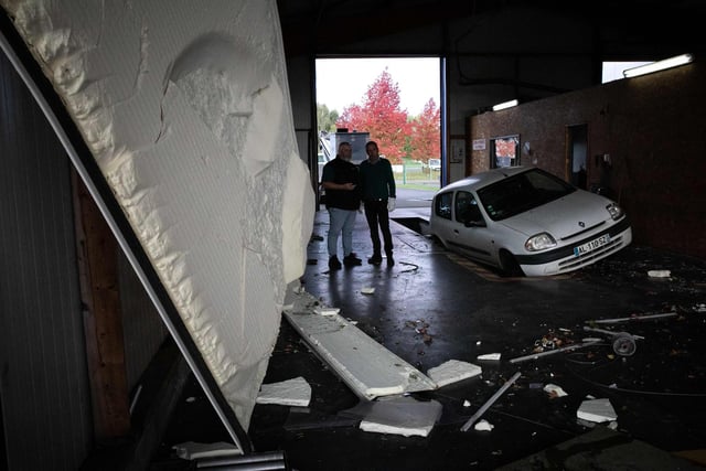 Owners of a automobile workshop look at damages in Beuzeville, northern France on October 24, 2022, after a tornado hit the region. (Photo by LOU BENOIST/AFP via Getty Images)