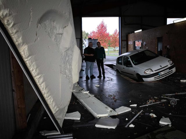 Owners of a automobile workshop look at damages in Beuzeville, northern France on October 24, 2022, after a tornado hit the region. (Photo by LOU BENOIST/AFP via Getty Images)