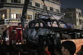 People watch as a vehicle that was hit by a drone strike, reportedly killing three people including a leader of a pro-Iran group, is carried away in Baghdad.