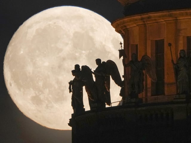 Sculptures of angels fixed at the St. Isaak's Cathedral are silhouetted on the full moon in St. Petersburg, Russia, Monday, June 13, 2022. (AP Photo/Dmitri Lovetsky)