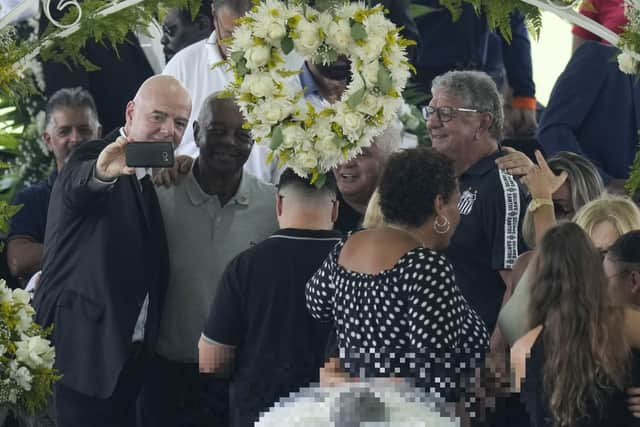 FIFA President Gianni Infantino, left, takes a selfie with Lima, a former Santos soccer player, and others, during the wake of the late Brazilian soccer great Pele, who lies in state, below, at Vila Belmiro stadium in Santos, Brazil, Monday, Jan. 2, 2023. (AP Photo/Andre Penner)