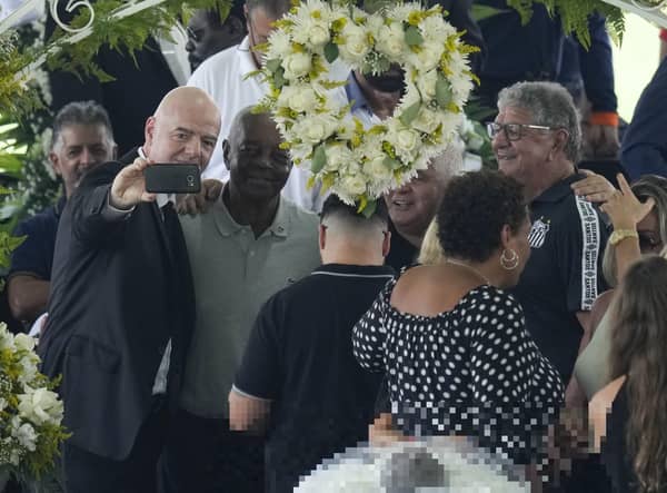 FIFA President Gianni Infantino, left, takes a selfie with Lima, a former Santos soccer player, and others, during the wake of the late Brazilian soccer great Pele, who lies in state, below, at Vila Belmiro stadium in Santos, Brazil, Monday, Jan. 2, 2023. (AP Photo/Andre Penner)