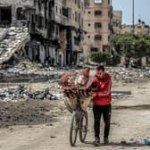 A man walks with a bicycle loaded with blankets and cushions past destroyed buildings along a street in Gaza City (Photo by -/AFP via Getty Images)