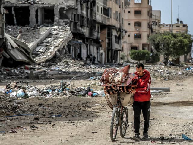 A man walks with a bicycle loaded with blankets and cushions past destroyed buildings along a street in Gaza City (Photo by -/AFP via Getty Images)