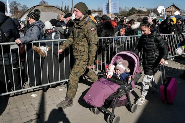 A young woman pushing a child in a buggy walks behind a Polish soldier as people wait for transportation after crossing the Ukrainian border into Poland, in Medyka, eastern Poland, on March 11, 2022. - Some 2.5 million people have fled Ukraine since Russia invaded two weeks ago, and another two million have been internally displaced by the war, the United Nations said on March 11, 2022. (Photo by Louisa GOULIAMAKI / AFP) (Photo by LOUISA GOULIAMAKI/AFP via Getty Images)