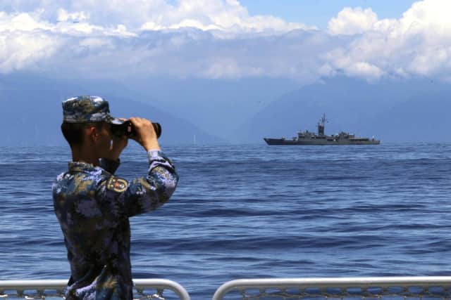 A People's Liberation Army member looks through binoculars during military exercises as Taiwan's frigate Lan Yang is seen at the rear on Aug. 5, 2022. China has reaffirmed its threat to use military force to bring Taiwan under its control.