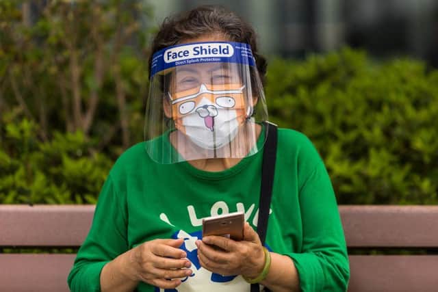 A woman wearing a face shield and mask uses her phone in a park in Hong Kong.