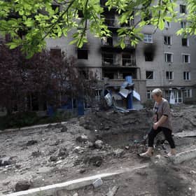 A woman walks past a shell crater in front of a damaged residential building in the town of Siversk, Donetsk region, on June 23, 2022, amid Russia's military invasion launched on Ukraine. -  via Getty Images