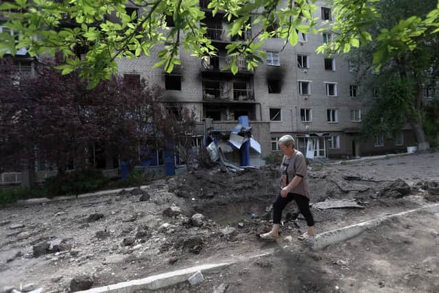 A woman walks past a shell crater in front of a damaged residential building in the town of Siversk, Donetsk region, on June 23, 2022, amid Russia's military invasion launched on Ukraine. - via Getty Images