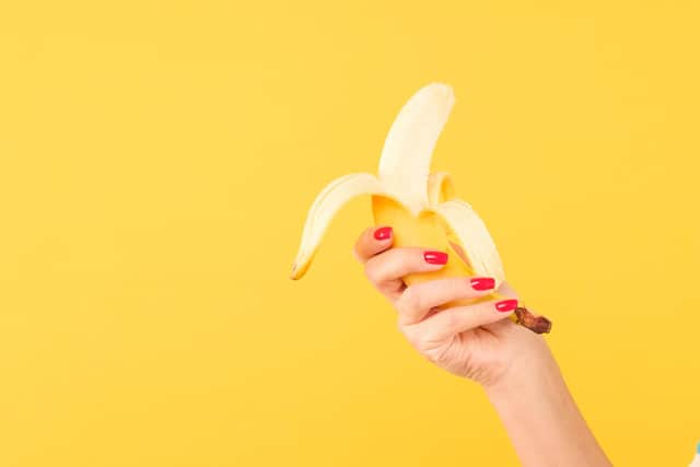 woman hand with red nail polish holding peeled banana on yellow background