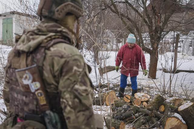 A Ukrainian serviceman watches Anna Pylypivna, one of the few residents who did not leave the frontline village of Novooleksandrivka, eastern Ukraine, handle firewood