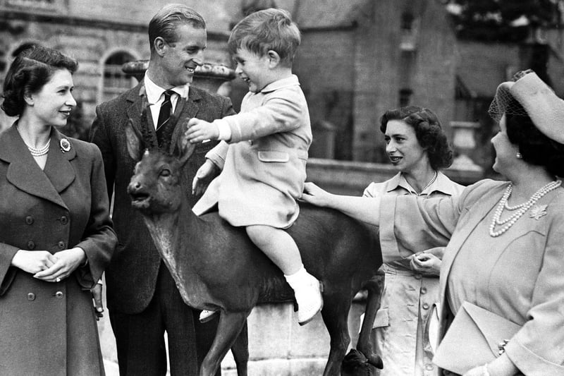 Prince Charles sitting on a statue watched by Princess Elizabeth, the Duke of Edinburgh, Princess Margaret and Queen Elizabeth while on holiday at Balmoral in August 1951.