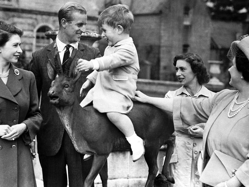 Prince Charles sitting on a statue watched by Princess Elizabeth, the Duke of Edinburgh, Princess Margaret and Queen Elizabeth while on holiday at Balmoral in August 1951.