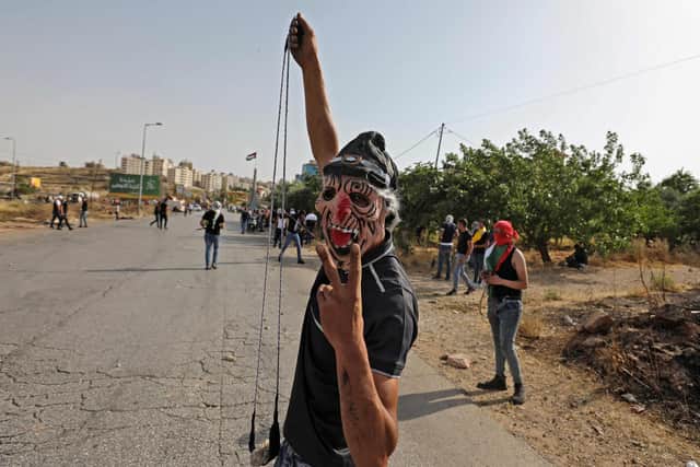 A Palestinian man wearing a mask flashes the victory sign as he lifts a sling used to hurl rocks, amid clashes with Israeli security forces close to the settlement of Beit El near Ramallah in the occupied West Bank (Picture: Abbas Momani/AFP via Getty Images)