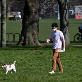 A man wearing a mask as a precautionary measure against covid-19 walks a dog on Clapham Common in south London on March 24