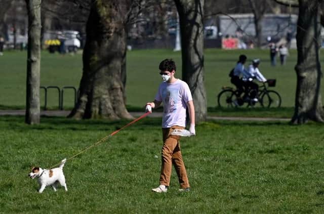 A man wearing a mask as a precautionary measure against covid-19 walks a dog on Clapham Common in south London on March 24