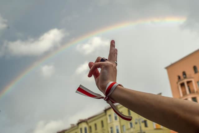 A person makes a V-sign wearing a bracelet with historical white-red-white colors of Belarus flag with a rainbow in the back as opposition supporters rally to protest against disputed presidential elections results in Minsk