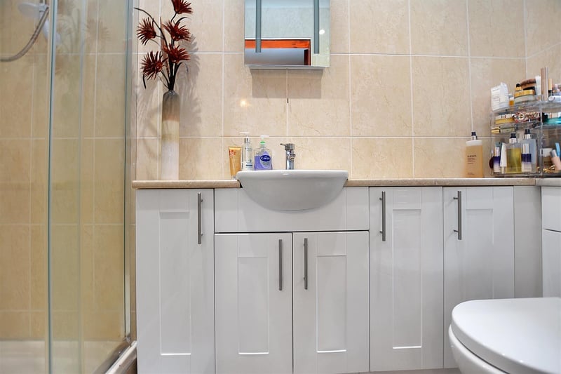With a modern three-piece suite of a tiled shower enclosure with electric shower, vanity unit with wash basin with storage cupboards beneath and low flush WC.