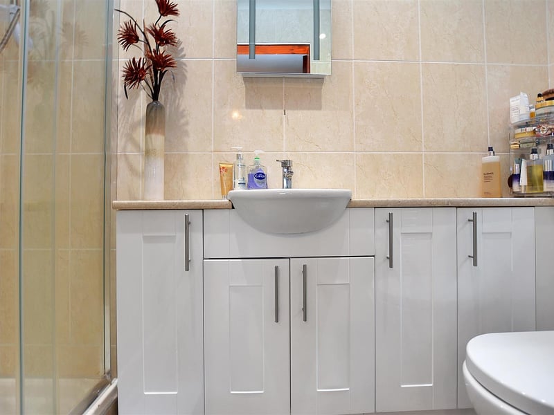 With a modern three-piece suite of a tiled shower enclosure with electric shower, vanity unit with wash basin with storage cupboards beneath and low flush WC.