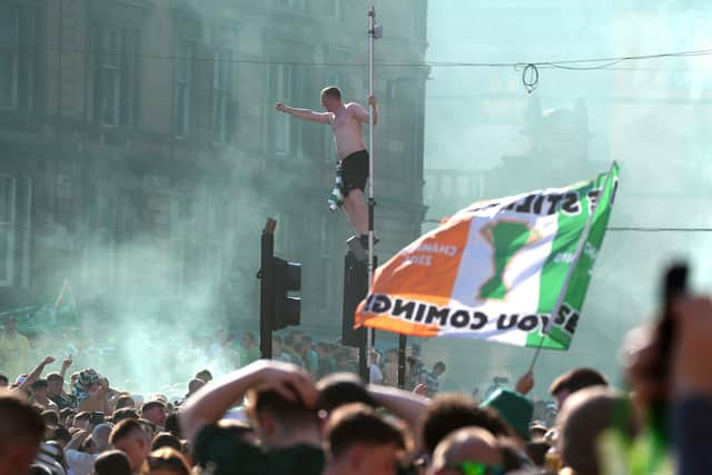 A Celtic fan perches on a set of traffic lights as supporters gathered at Glasgow Cross on Saturday to celebrate winning the Premiership (Picture: Andrew Milligan/PA Wire)