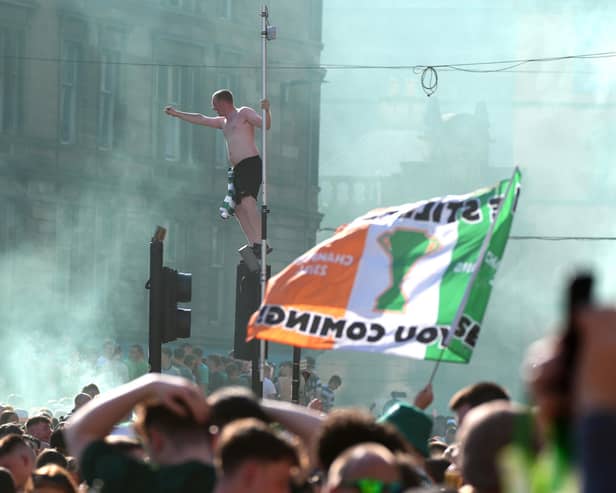 A Celtic fan perches on a set of traffic lights as supporters gathered at Glasgow Cross on Saturday to celebrate winning the Premiership (Picture: Andrew Milligan/PA Wire)