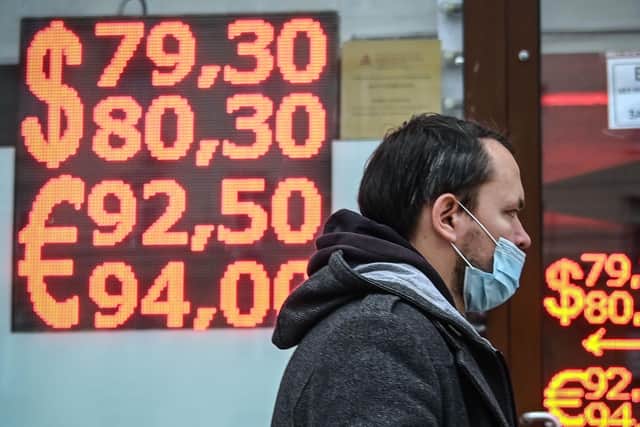 A man wearing a face mask below his nose walks past a screen displaying the currency exchange rates in Moscow (Picture: Alexander Nemenov/AFP via Getty Images)