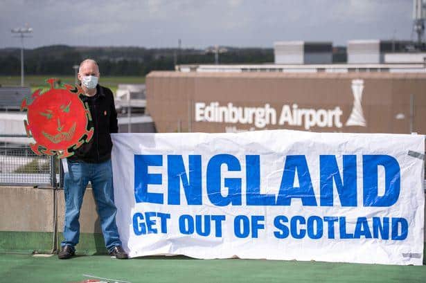An activist stages protest at Edinburgh Airport, demanding English tourists do not travel to Scotland.
