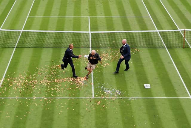 A protester is challenged by security on court 18 after a Just Stop Oil protest using orange confetti and a jigsaw puzzle during the Women's Singles first round match between Katie Boulter of Great Britain and Daria Saville of Australia.