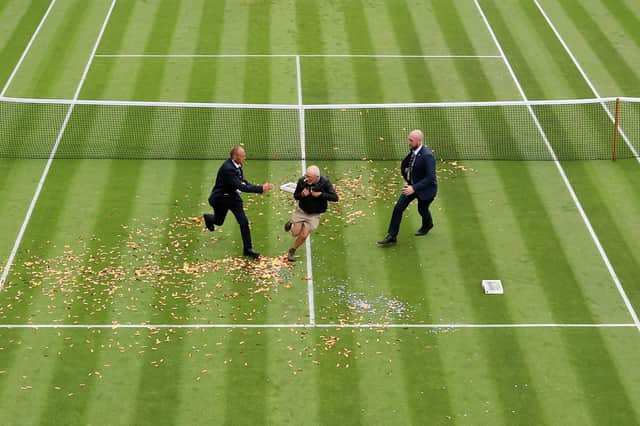 A protester is challenged by security on court 18 after a Just Stop Oil protest using orange confetti and a jigsaw puzzle during the Women's Singles first round match between Katie Boulter of Great Britain and Daria Saville of Australia.