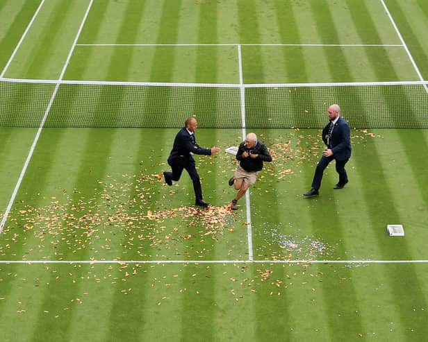 A protester is challenged by security on court 18 after a Just Stop Oil protest using orange confetti and a jigsaw puzzle during the Women's Singles first round match between Katie Boulter of Great Britain and Daria Saville of Australia.