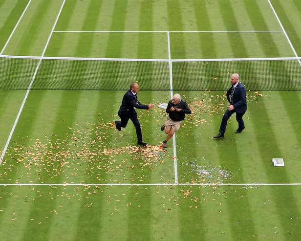 A protester is challenged by security on court 18 after a Just Stop Oil protest using orange confetti and a jigsaw puzzle during the Women's Singles first round match between Katie Boulter of Great Britain and Daria Saville of Australia.