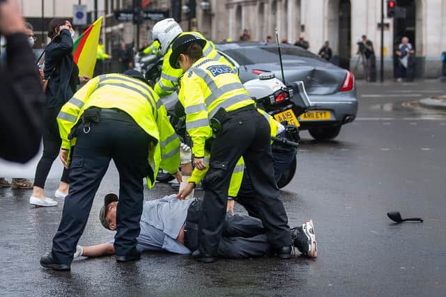 Police detain a man after he ran in front of Prime Minister Boris Johnson's car (in background with dent) as it left the Houses of Parliament, Westminster.