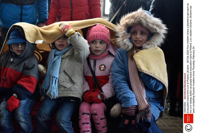 Four children share a blanket to get warm at the Lviv railway station as people board evacuation trains to Poland, Lviv, western Ukraine. Photo: Ukrinform/Shutterstock