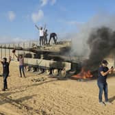 Palestinians celebrate by a destroyed Israeli tank at the Gaza Strip fence. Picture: Hassan Eslaiah/AP