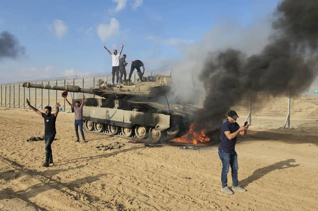 Palestinians celebrate by a destroyed Israeli tank at the Gaza Strip fence. Picture: Hassan Eslaiah/AP