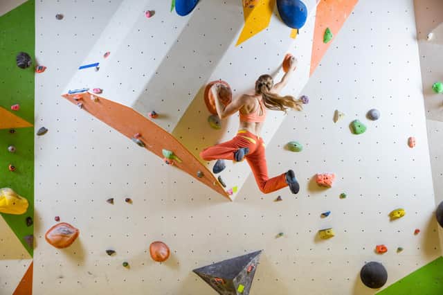Young woman jumping on handhold in indoor bouldering gym Pic:Andrey Bandurenko/Adobe