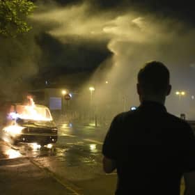 Firefighters use a water hose on a burnt car in Nanterre, outside Paris,