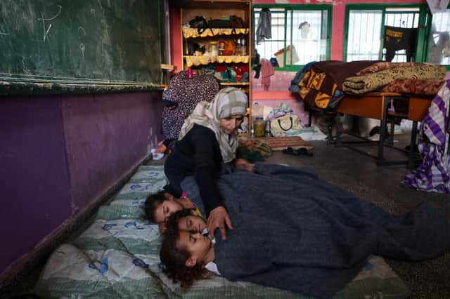 EDITORS NOTE: Graphic content / TOPSHOT - A Palestinian woman covers sleeping children with a blanket as they take refuge in a United nations school, in the Rafah refugee camp, in the southern of Gaza Strip on October 14, 2023, as fighting between Israel and the Hamas movement continues for the eighth consecutive day in the Gaza Strip enclave. Palestinians sought refuge on October 14, 2023, after Israel warned them to evacuate the northern Gaza Strip before an expected ground offensive against Hamas, one week after the deadliest attack in Israel's history. (Photo by MOHAMMED ABED / AFP) (Photo by MOHAMMED ABED/AFP via Getty Images)
