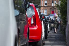 People struggle to pass cars parked on a narrow street pavement