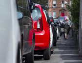 People struggle to pass cars parked on a narrow street pavement