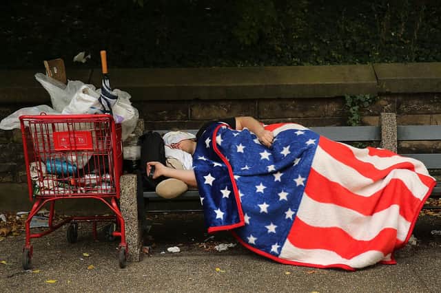 A homeless man sleeps under an American flag blanket on a park bench in Brooklyn, New York City (Picture: Spencer Platt/Getty Images)