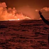 A local resident watches smoke billow as the lava from an volcanic eruption on the Reykjanes peninsula 3 km north of Grindavik, western Iceland,  coloured the night sky orange.