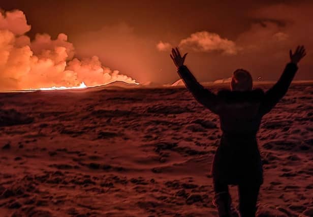 A local resident watches smoke billow as the lava from an volcanic eruption on the Reykjanes peninsula 3 km north of Grindavik, western Iceland, coloured the night sky orange.