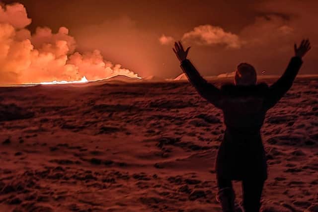 A local resident watches smoke billow as the lava from an volcanic eruption on the Reykjanes peninsula 3 km north of Grindavik, western Iceland,  coloured the night sky orange.