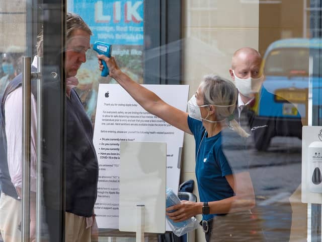 A retail worker  takes the temperature of a customer entering the Apple Store on Princes Street in Edinburgh on June 29, 2020