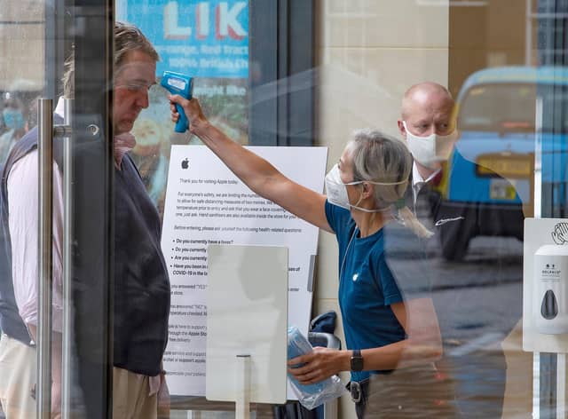 A retail worker  takes the temperature of a customer entering the Apple Store on Princes Street in Edinburgh on June 29, 2020