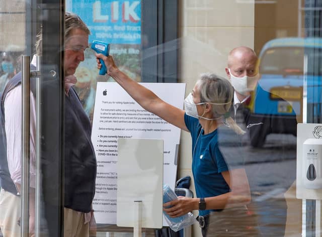 A retail worker  takes the temperature of a customer entering the Apple Store on Princes Street in Edinburgh on June 29, 2020