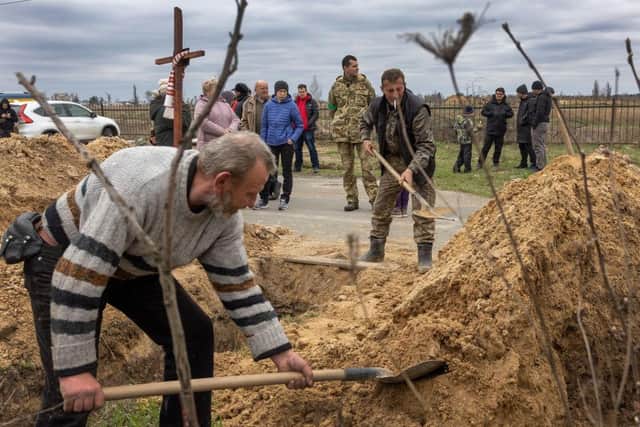 Ukrainian grave diggers shovel soil into an open grave in Bucha, Ukraine. Hundreds of Ukrainians killed during the Russian invasion in Bucha are being laid to rest in the cemetery.